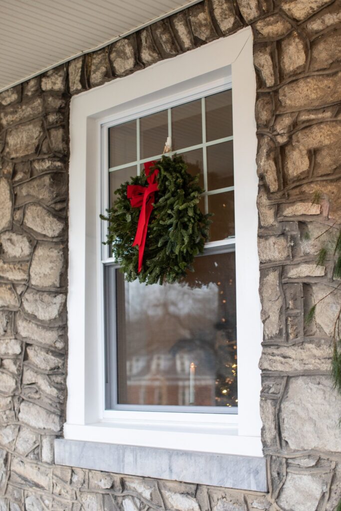A wreath is hung on a window using an adhesive hook for exterior holiday decorating without the damage.