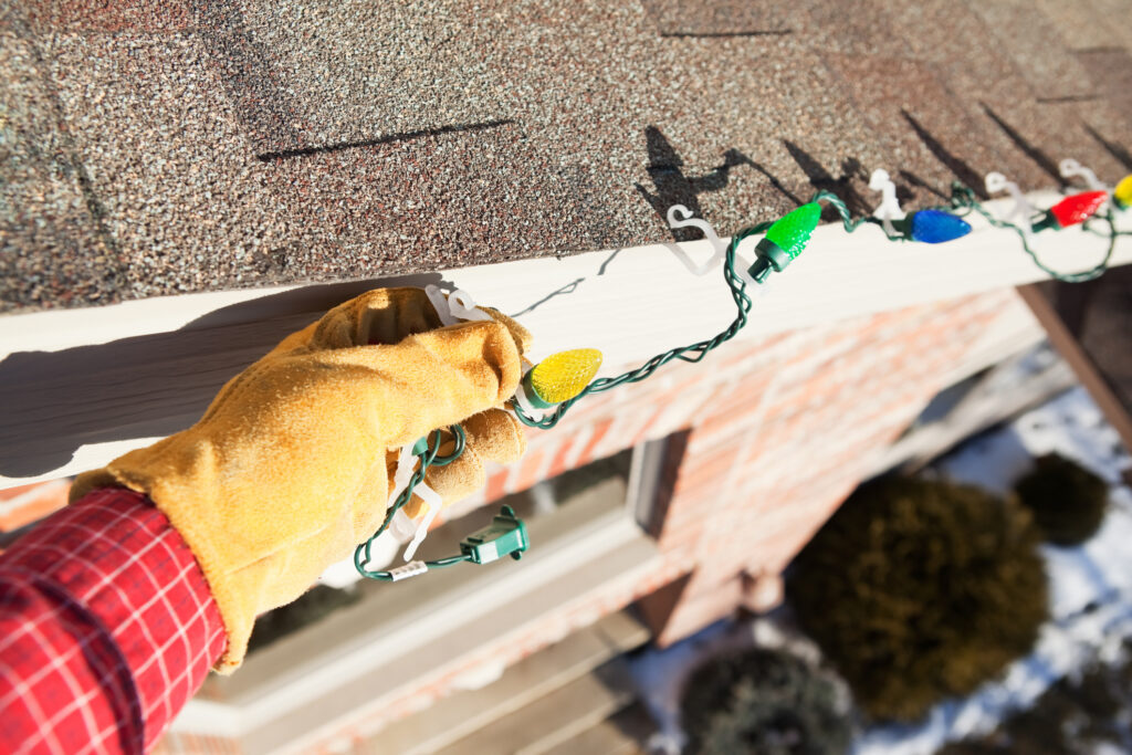 A homeowner installing holiday lights using plastic clips that do not cause damage to the roof or gutters.