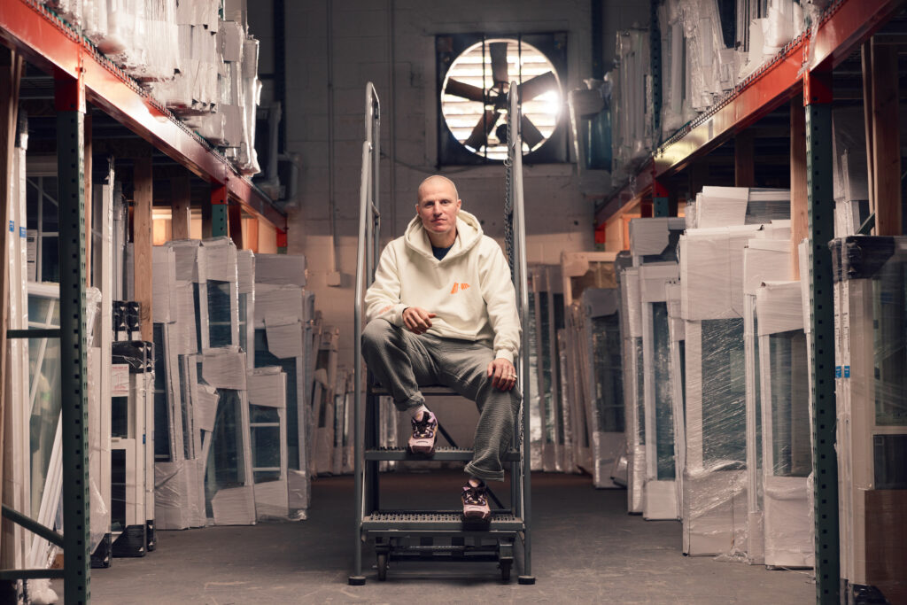 Jimmy Gorecki sits in POWER's Warehouse modeling the POWER x Standard Issue cream colored Quest sweatshirt.