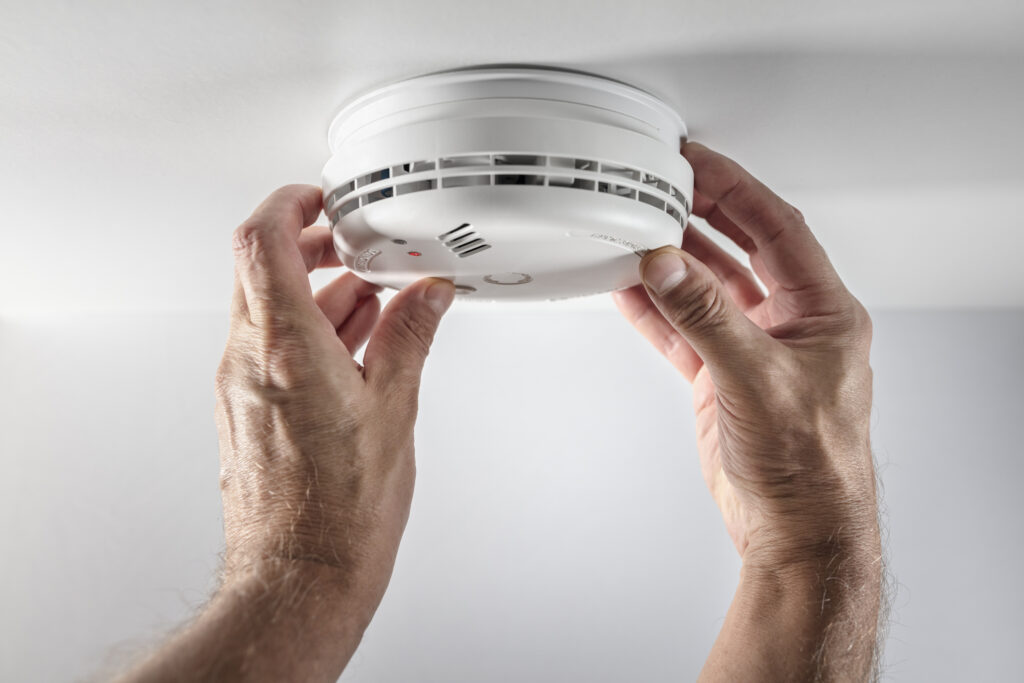 closeup of hands checking a smoke alarm on a ceiling.