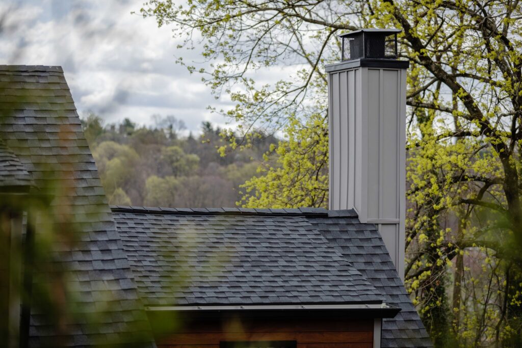 a closeup of a chimney and grey roof surrounded by trees.