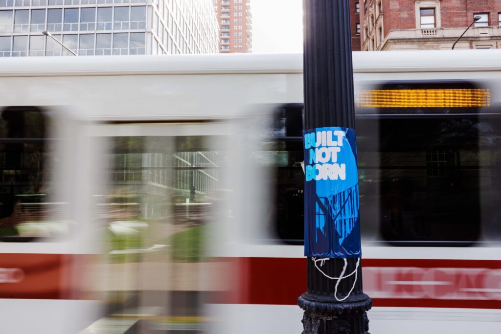 Photo of a street post with "Built not Born" sign, with bus passing behind.