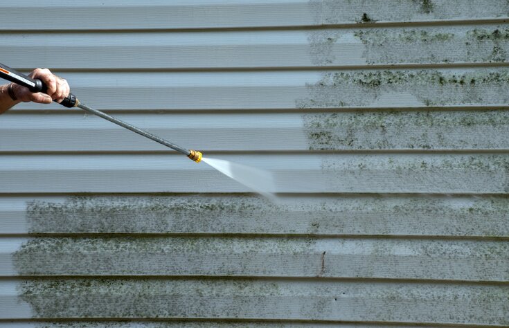 A homeowner pressure washing dirty siding.