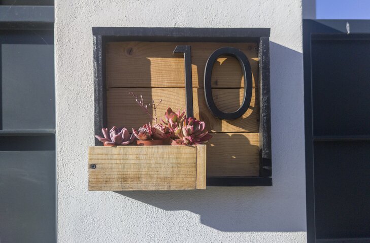 Modern matte black house numbers within a wood box with succulent plants.