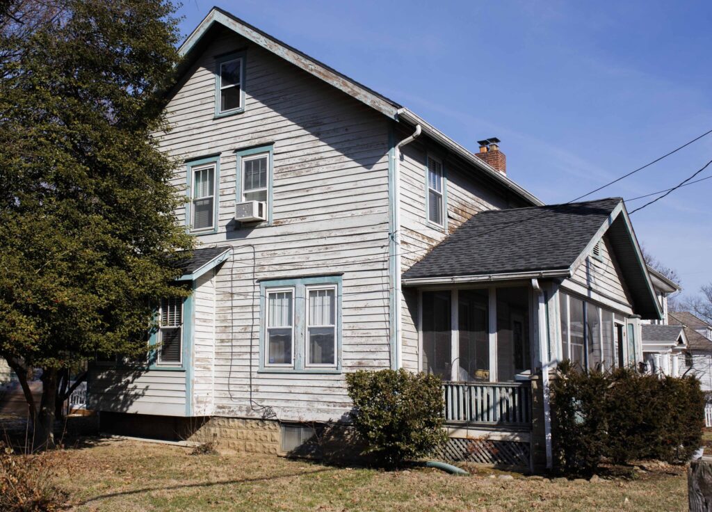 A white, multi-story house with dirty and rotting siding, pre-POWER siding installation.