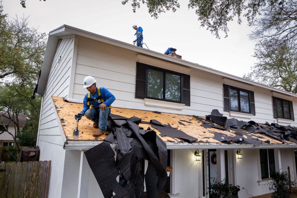 Men in blue POWER uniforms on roof, scraping off the tile exposing the wooden frame underneath