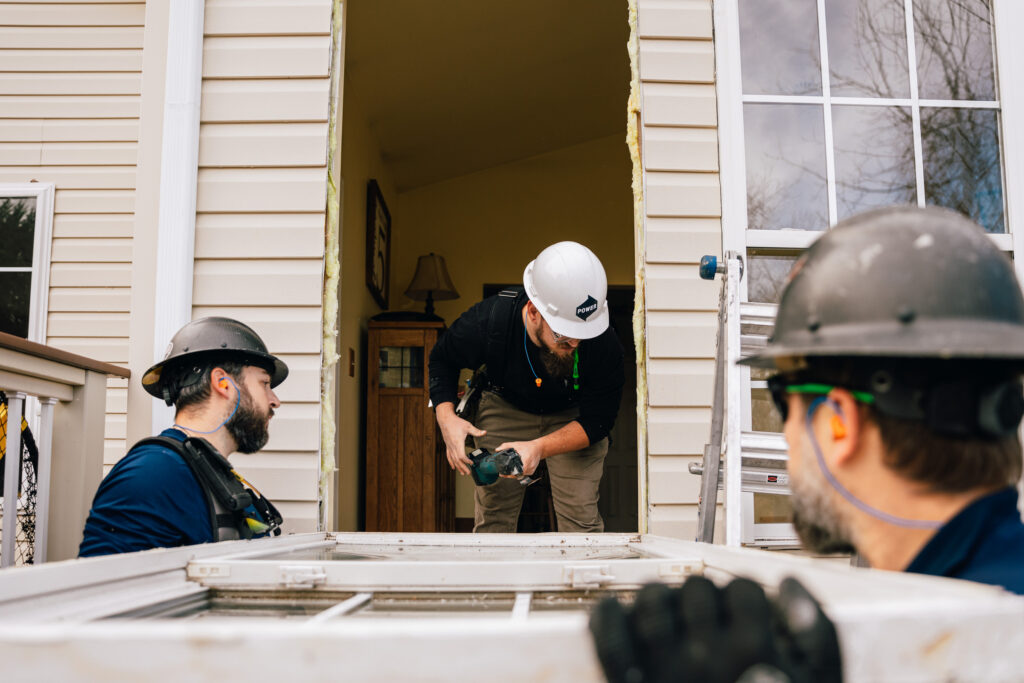Power installers work to install a new door on a house.