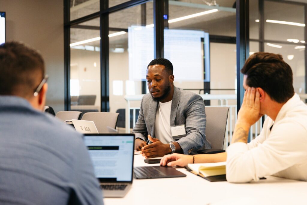 Three employees sit together at conference table discussing work.