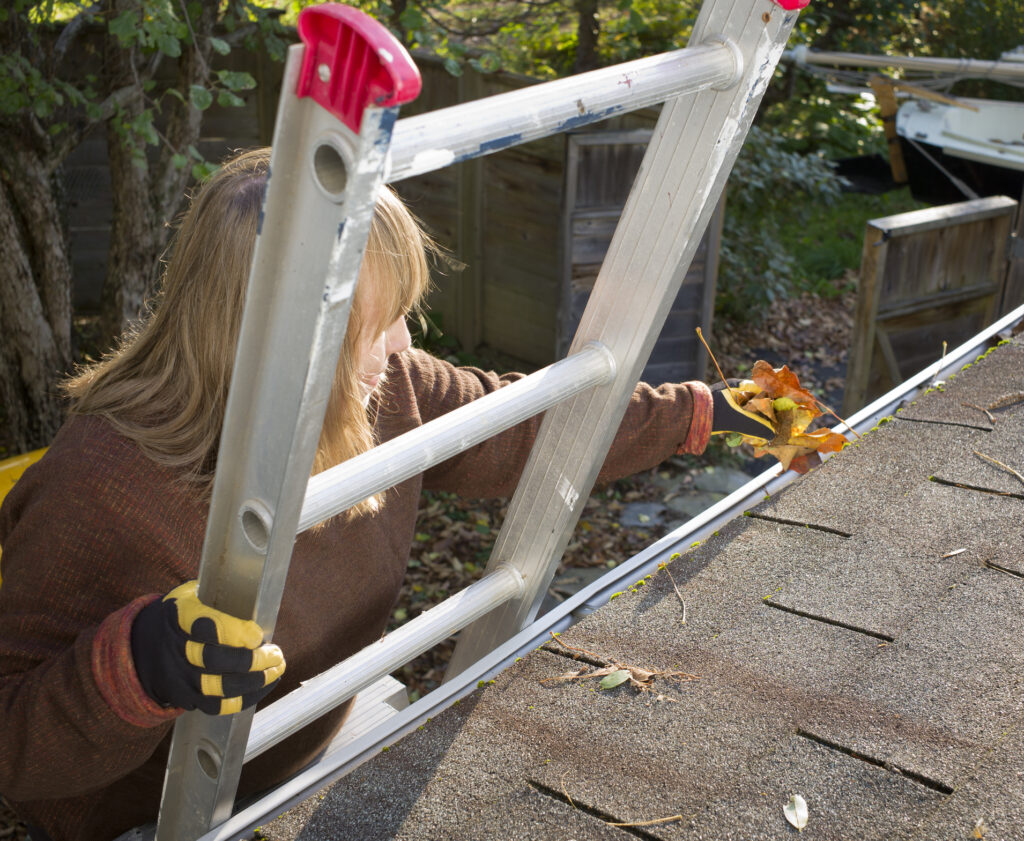 Woman standing on ladder cleaning gutters.